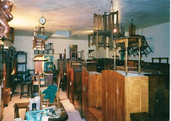 The interior of India Street Antiques after opening in October, 1991. This photo shows the front warehouse and was taken before demolition of the back wall to include the back warehouse as part of the showroom as it is today. 

Just as today, the shop is shown packed to the rafters with armoires lined up in rows and chairs hanging from the ceiling!