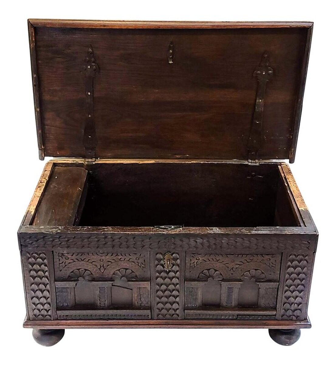 Spanish Renaissance period carved oak arcón with iron and brass mounts. Antique chest from the 1600s is peg constructed of oak wood. The lid is solid burl figured oak attached to the carcass with wrought iron diamond tipped strap hinges on the underside. The front panels show carvings of foliated spandrels over arcading arches cupping floral fans. The arches stand on plinth bases. The original key fits through a chased brass escutcheon sporting a foliated scroll and lozenge motif. The carcass rests upon four turned oak bun feet. The side panels are fitted with twisted wrought iron bail handles. The handles indicate this may have been built for use as a traveling trunk or campaign chest. The back is of a plain board. The interior is fitted with a hinged-lid box on the top left side for storage of candles and other small objects. Outer surfaces are finished with hand rubbed paste wax.
