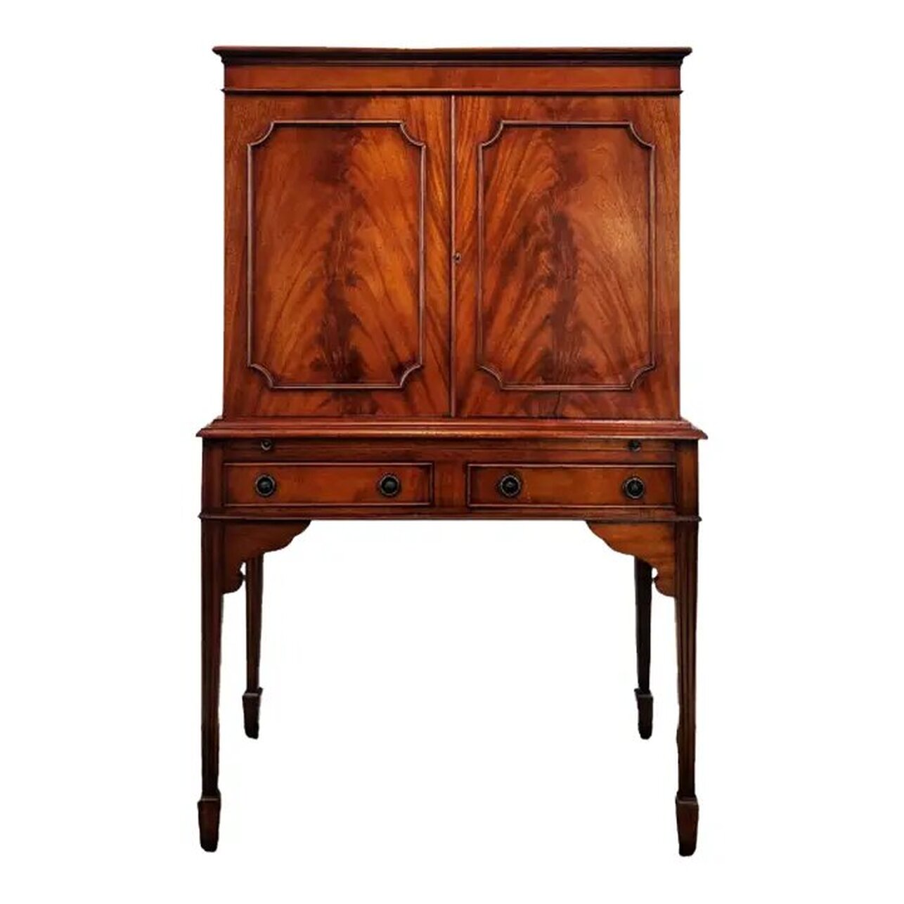 Georgian style mahogany cocktail cabinet was built by Bevan Funnell Ltd., Beach Road, Newhaven, Sussex, England. Bevan Funnel was established in 1945 and is known for bespoke and classically influenced furniture designs. This drinks cabinet was constructed from mahogany wood in the mid-to-late-20th-century. The top and sides feature ribbon figured mahogany and the door fronts feature flame, or crotch cut, mahogany. Under the flat top with molded edge is a cabinet with two locking doors lined on the interior with plain sycamore wood. The interior of the cabinet is lined with figured sycamore wood and mirrored on the back and bottom. A light fixture at top turns on when plugged in. The interior also contains a removable shaped sycamore wood shelf. The cabinet comes with a key. Below the cabinet is a pull-out shelf for use as a cocktail prep station. The shelf easily slides forward with a pull on the two round brass knobs. Two frieze drawers are located under the pull-out shelf and may be opened with a tug on the circular ring pulls over round decorative escutcheons. Curvy supports are placed under the front apron where the front legs attach. All four legs are square fluted tapers ending in spade feet. All hardware is solid brass. This mahogany cocktail cabinet will complement interiors with elements of Georgian, Sheraton, Hepplewhite, Chippendale, Queen Anne, Victorian and Edwardian Sheraton styles. The cabinet will blend nicely with your Bevan Funnell ranges