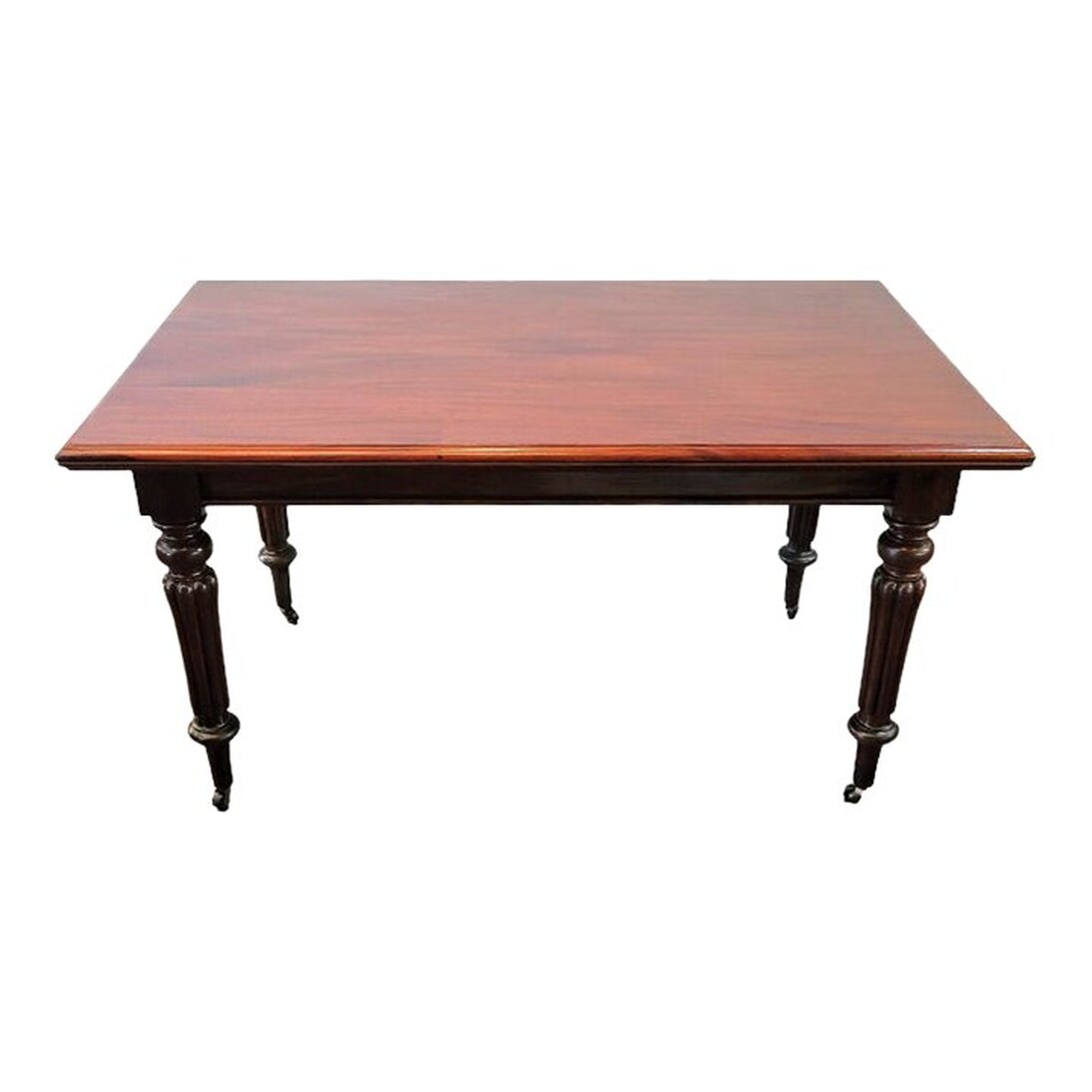 Antique Santo Domingo mahogany table attributed to Gillows of Lancaster works perfectly as a library table, dining table, café table, writing desk, and work table. The molded-edge rectangular table top shows off the beautiful qualities of Santo Domingo mahogany wood - the rich color, burled figure, and distinctive ribbon grain common to mahogany. The plain apron has a molded bottom edge. The four corner blocks surmount the turned, ringed, and tapered legs. The legs are reeded through the middle. The legs end in tapered arrow feet on castors.
