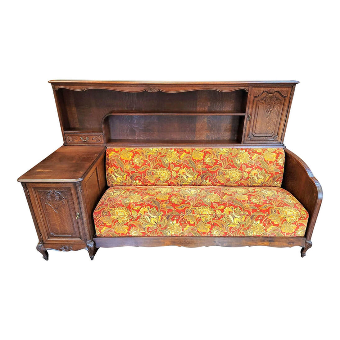 Antique Cozy Corner consists of an upholstered sofa bench, shelves, and cabinets. Cozy Corners were designed and manufactured mainly in Belgium, France, Holland, and England from about 1898 through to the 1960s. Cozy Corners were made in many styles, including Arts & Crafts, Art Nouveau, Art Deco, and the Louis style offered here. This Cozy Corner was made in Liège, Belgium circa 1920. The delicate carving in the oak wood is in the Louis XV Regency style of Liège, Belgium. The refined foliate flourishes, gentle curves, and naturalistic floral and shell motifs are influenced by the Rococo and resemble French wall paneling. These are hallmarks of Liège style ornamentation and carving on furniture. The firm spring sofa is nicely upholstered in a hardy velveteen fabric with a red ground on which are printed leaves and flowers in fall colors of yellows, golds, browns, grays, black, and tans. The sofa is surrounded by quarter-sawn, or