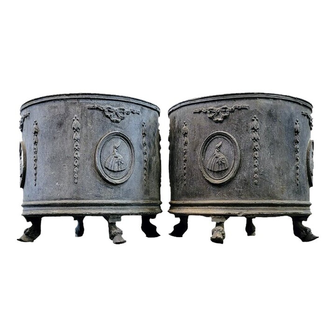 Antique cast lead round garden planters date to the 1910s and were made in England. The circular planters stand on four hairy pied-de-biche ( deer's foot ) hoof feet. The decorative motifs include ribbon bows and flower husk pendants framing cartouches of women in antebellum gowns and bonnets. The motifs are repeated four times around the body of the planter.