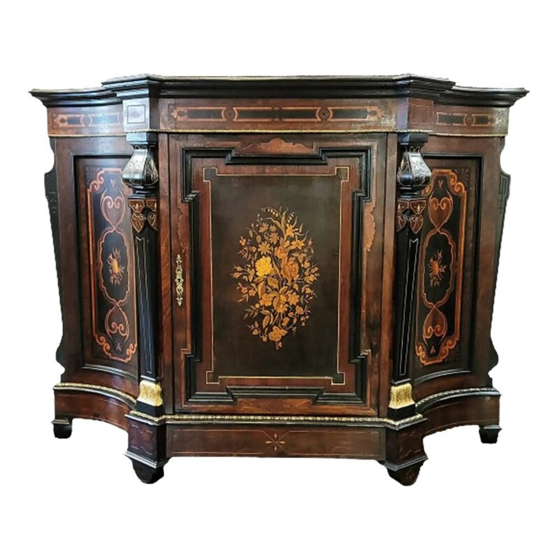 Victorian credenza and music cabinet has a shaped top with a molded edge enhanced with gilt bronze trim. The frieze is decorated with marquetry strapwork. The bottom edge is enhanced with gilt bronze trim. The case is made of maple wood with inlaid rosewood veneers and an ebony finish simulating Asian lacquer. Two decorative supports are on the front of the credenza at either side of the single door cabinet at center. The supports are incised gilded and ebonized wood. The central cabinet door is decorated with an intricate molded frame into which is set a rich marquetry panel of different exotic woods forming a bouquet of flowers. The interior of the door is paneled with birds-eye maple wood. The inset hinges and lock are made of solid brass. The keyhole escutcheon on the door is in an openwork arabesque form. The interior of the cabinet is paneled with maple wood and is fitted with a substantial solid maple wood removable shelf. The concave side panels also feature rich marquetry motifs of musical instruments framed by anthemia. Two more decorative supports are at each side back. They are incised and ebonized wood. The base is shaped to reflect the top, has a molded top edge enhanced with gilt bronze trim, and an incised apron. The four demi-lune feet are placed under molded top edges and feature incised decoration. The back is framed panel constructed with an ebonized finish. Available from India Street Antiques, San Diego.