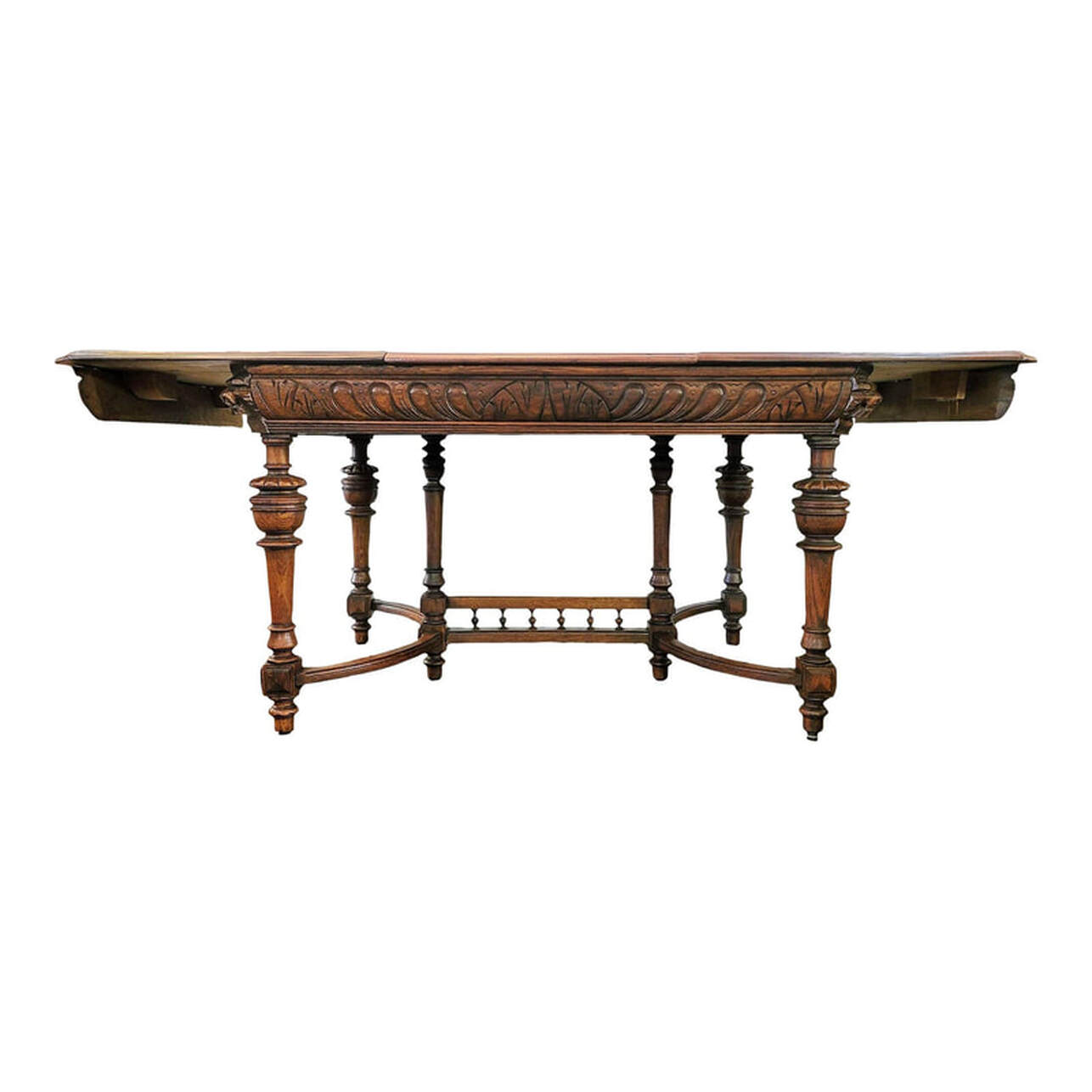 Well-crafted, beautiful, and sturdy carved oak dining table made in Mechelen, Antwerp, Belgium, circa 1900. The closed table top is built from quarter-sawn oak wood, sometimes called tiger oak for the golden rays in the figure. The table top shows a seam down the middle. This is where the two ends of the top open for leaf placement. The table top edges are molded and match the molding on the ends of the table leaf. The corners are canted. The table leaf is made from burl figure oak wood and has a finished molded edge to match the two halves of the table top. The leaf is placed in between the two halves of the table top to extend the length of the table. Underneath the center top on each side are round brass latches that lock the table top in place. We installed these latches. They easily unlatch to open the table for leaf placement. The steel plate at center is part of the old latching system and shows how a bar would have run through to hold the table top in place. The table apron is embellished with carved arches and gadrooning with a molded bottom edge. The four canted corners are inset with carved blocks featuring projecting lion's heads. The holes through the mouths indicate the lion's heads once had hanging rings, a mask and handle motif dating back to ancient Rome and representative of strength, courage, and majesty. The four oak corner legs and the two center legs are tapered over square blocks embellished with layered geometrics, turned, ringed, and carved, and end in turned, ringed arrow feet. The Flemish style curved stretchers on each end attach to the square blocks on the legs. The trestle is set between the two center legs and features a gallery of six turned wood Greek urn or amphorae shaped elements. SIZE: CLOSED: 50