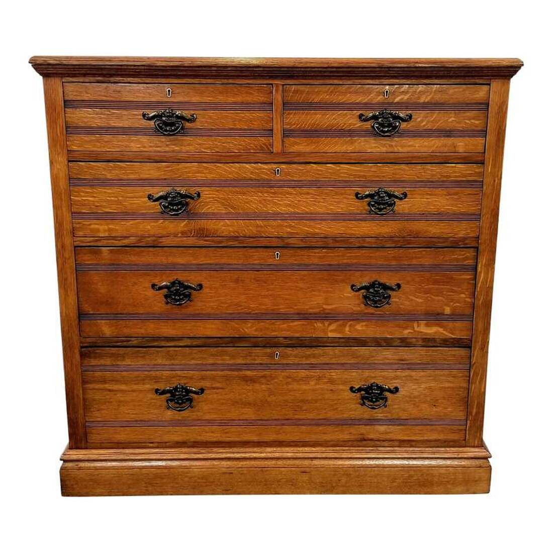 Original Medieval-influenced English Arts & Crafts oak chest of five drawers based on an 1874-1876 creation by Owen William Davis for James Shoolbred & Co. Chest has two small side-by-side drawers at top followed by three full-length drawers below. The drawers are accessed by tugging on the copper-plated Arts & Crafts pulls.  Dresser is constructed with quarter sawn (