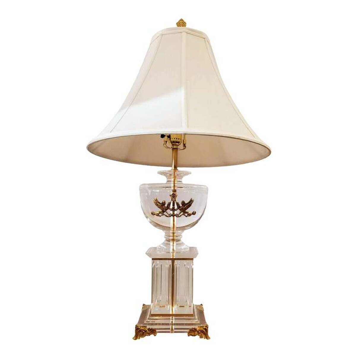 Neoclassic style table lamp in the form of a fluted column pedestal on gilt acanthus scroll feet surmounted by a lebes urn fronted with a gilt pair of sphinx on either side of a lyre. The base material is clear acrylic thermoplastic resin, known by the trade name Lucite. The brass spacers and hardware are brass. The light turns on via a 3-way rotary lamp switch.