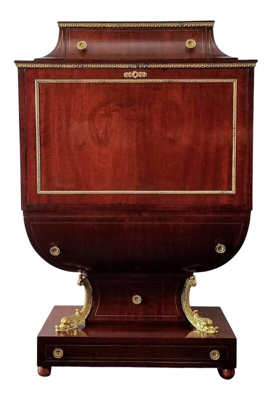 Replica of early 19th century secretary, or fall front, desk ( secrétaire à abattant ) in the French Empire / Viennese and Austrian Biedermeier style finished with mahogany veneers and chased brass mounts. Under the chased brass trim at the top is a single drawer with two chrysanthemum chased pulls and inlaid brass banding. Brass banding is also inset to the sides of the drawer. The drop front is located below more chased brass trim. The panel is framed with chased brass trim and there is a chased brass key scutcheon at top. The interior is fitted with eight small storage drawers - four on either side of the central cabinet. The drawers feature inset brass banding and laurel wreath drop pulls. Below the central cabinet is one long drawer with inlaid brass banding and two laurel wreath drop pulls. The shaped door at center is framed and inlaid with brass banding. The open door reveals a hidden cocktail cabinet with one glass shelf and mirrored back. The writing and work surface of the drop front panel is inset with embossed gold decoration on green leather. The possum belly drawer below the drop panel is edged with inset brass banding and has two chrysanthemum chased brass pulls. The base has one shaped drawer with a chrysanthemum chased brass pull and inlaid brass banding. On each side of this drawer are gilt dolphins. At the bottom, above the bun feet, is one long drawer with two chrysanthemum chased pulls and inlaid brass banding.