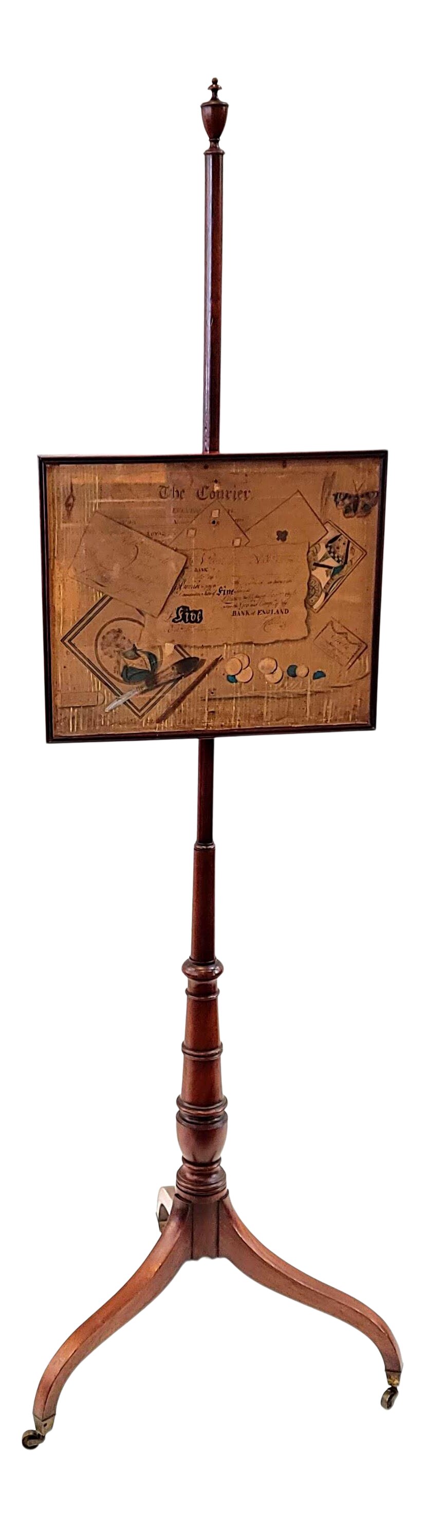 English Regency turned mahogany adjustable pole fire shield in the Georgian style of the mid-to-late-18th-century.  The pole is turned ringed mahogany with an urn finial at top.  The pole is attached to a trio of sabre legs ending in squared brass caps and casters.  The banner shield is a rectangular mahogany wood frame with a glass front housing original ink, watercolor, and pastel gambling art. 